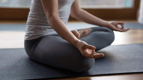 Person sitting cross-legged on a mat with hands resting on knees